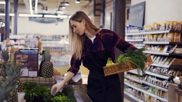 Női dolgozó fekete kötényben rendezi zöldek szupermarketben, eltávolítja az elkényeztetett — Stock videók