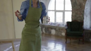 Geniş bir tuvalin önünde elinde büyük bir fırça tutan kadın.