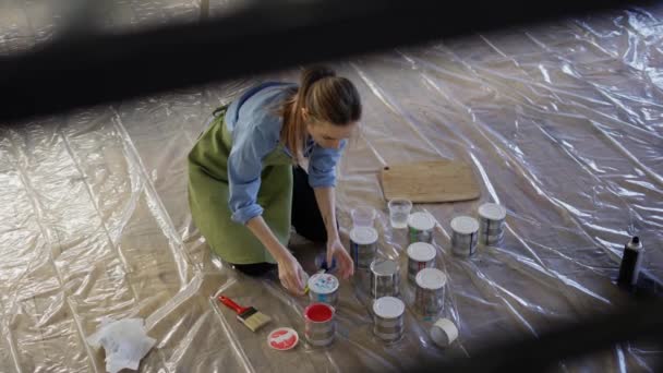 工房の女性は床に金属瓶の塗料の異なる色を開きます — ストック動画