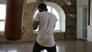 Afro-Amerikan boksör spor salonunda kum torbasına yumruk atıyor.