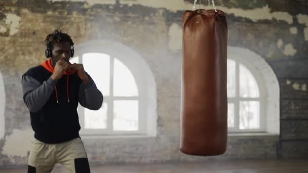 Afro american young male boxer practicing shadow boxing in headphones in bright hall — Stock Video