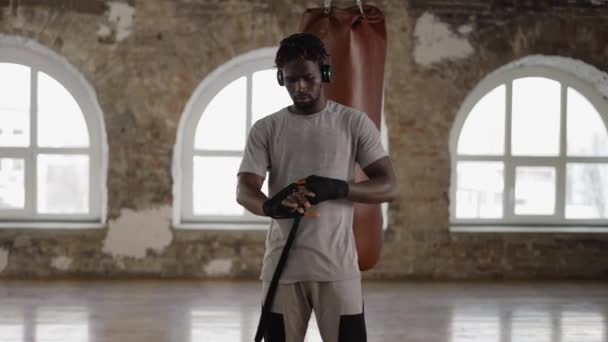Afro amerykański bokser owija ręce czarnym bandażem w bokserskim studio — Wideo stockowe