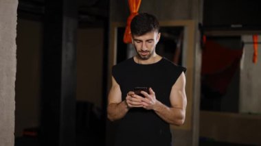 Genç adam karanlık spor salonunda telefon kullanıyor.