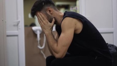 Soyunma odasında oturan yorgun ve üzgün bir adamın portresi.