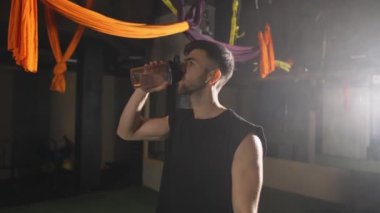 Sert adam karanlık spor salonundaki şişeden su içiyor.