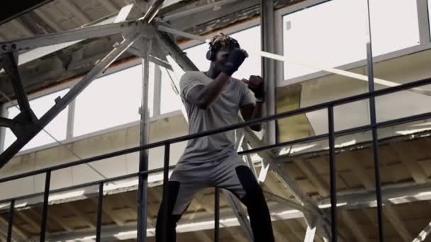 Boxeador masculino joven afroamericano practicando boxeo de sombras alrededor de las estructuras metálicas en interiores — Vídeos de Stock