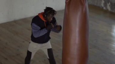 Afro-Amerikan boksör spor salonunda ağır topa vuruyor.
