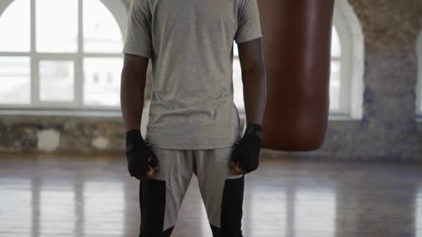 Afro americký boxer se dívá na kameru, zatímco stojí v blízkosti boxovací pytel — Stock video