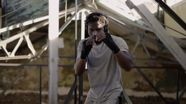 Boxeador joven afroamericano practicando boxeo de sombras alrededor de las estructuras metálicas — Vídeo de stock