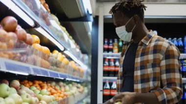 Süpermarkette durup alışveriş sepetine elma koyan Afrikalı Amerikalı bir adam.