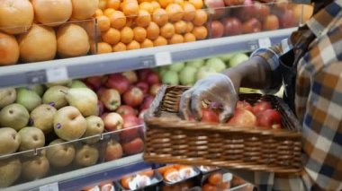 Market işçisi raflardan elma alıyor, meyve reyonundaki rafları yeniden düzenliyor.