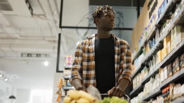 Mężczyzna pchanie wózek wzdłuż alejki supermarketu spożywczego, niski kąt widzenia — Wideo stockowe
