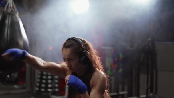 Concentrated boxer performing active punching in bandages, wearing headphones — Stock Video