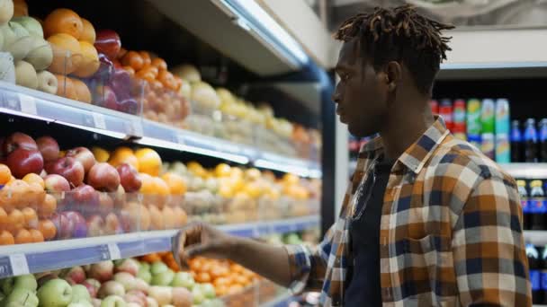 Yakışıklı Afrikalı Amerikalı adam süpermarkette duruyor ve elma topluyor. — Stok video