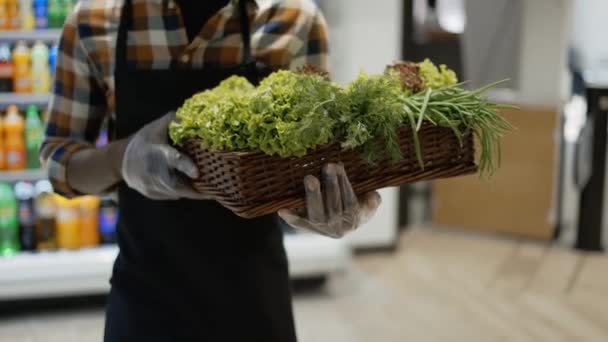 Männlicher, nicht erkennbarer Arbeiter in Handschuhen im Geschäft geht mit einem Korb voller Grünzeug spazieren — Stockvideo