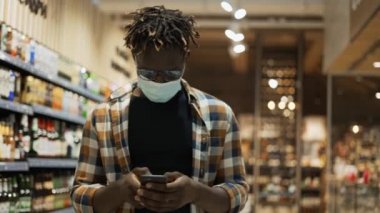 Mağazada akıllı telefon yürüyüşleriyle meşgul olan maskeli Afro-Amerikalı adam.