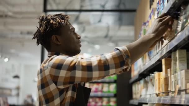 Африканский американский рабочий в фартуке, расставляющий полки с продуктами в продуктовом магазине, вид под низким углом — стоковое видео