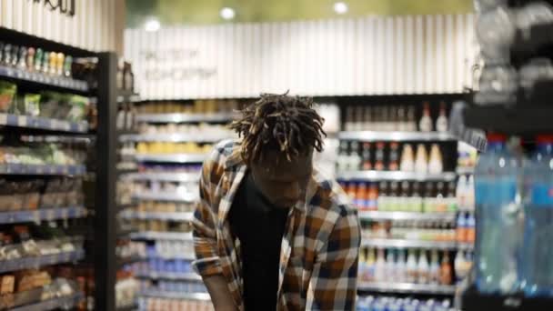 Человек толкает тележку вдоль супермаркета в магазине, берёт бутылку воды — стоковое видео