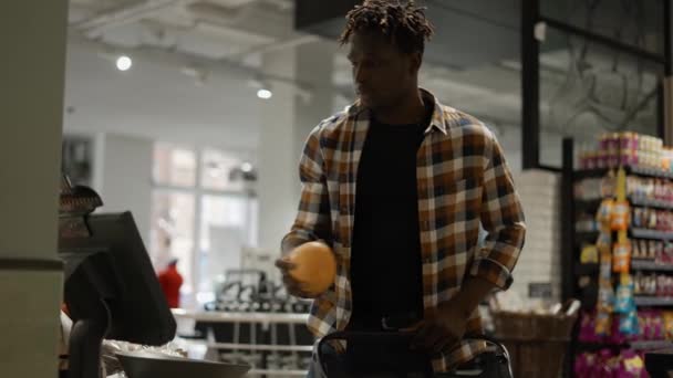 Homem com carrinho de compras pesando frutas nas balanças do supermercado — Vídeo de Stock