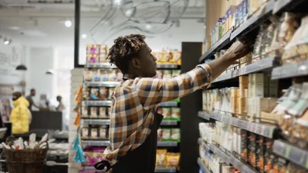 Trabalhador afro-americano em avental organizando prateleiras com produtos na mercearia — Vídeo de Stock