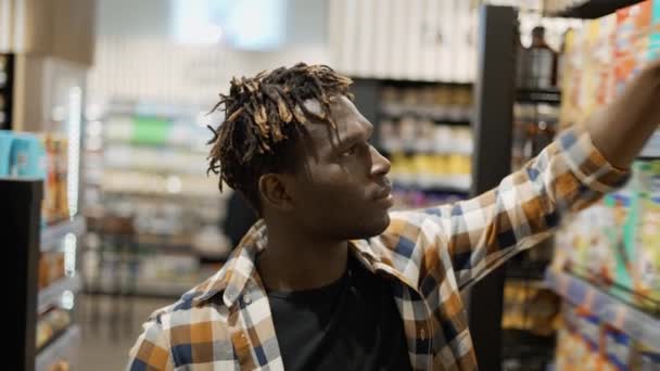 Красивий афроамериканський хлопець вибирає кукурудзяні пластівці в продуктовому магазині — стокове відео