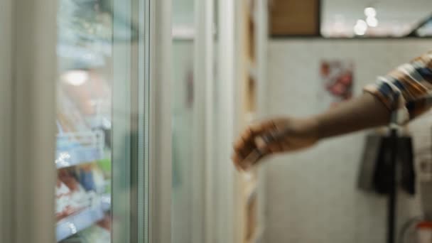 Bir alışverişçi marketin buzdolabından yiyecek seçer. — Stok video