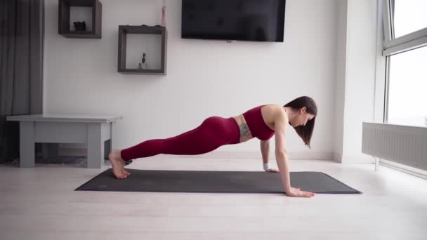 Fiatal sportos nő push-up gyakorlatokat végez a szőnyegen a nappaliban — Stock videók