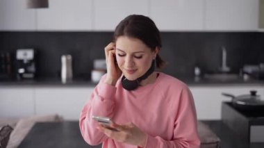 Kulaklıklı güzel bir kadın mutfakta dans ediyor ve müzik dinliyor.