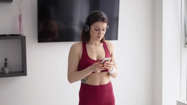 Mulher em fones de ouvido colocando música no celular para treino — Vídeo de Stock