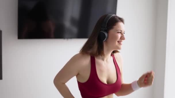 Mujer morena feliz en auriculares bailando en casa — Vídeo de stock