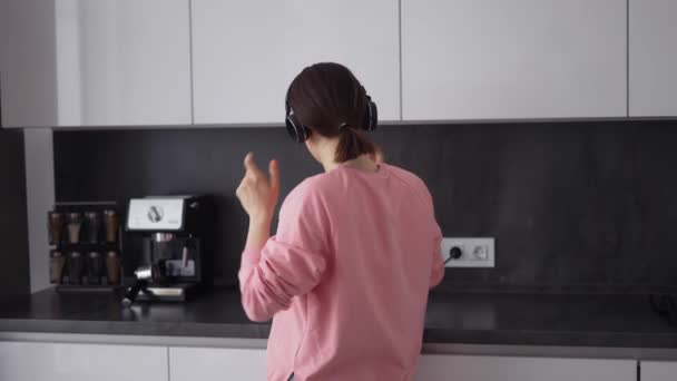 Πορτρέτο του κοριτσιού που ποζάρει στην κουζίνα, ακούγοντας τραγούδια στα ακουστικά — Αρχείο Βίντεο