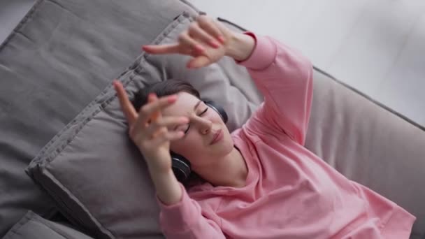 Mulher relaxante em sofá confortável com os olhos fechados usando fones de ouvido — Vídeo de Stock