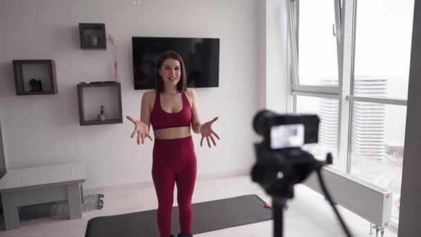 Genç bir kadın fitness eğitmeni kamerada ev egzersizleri üzerine bir ders kaydediyor. — Stok video