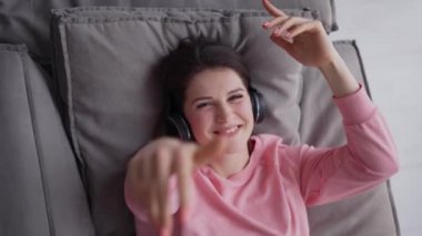 Kadın rahat koltukta oturup kulaklıkla müzik dinliyor.