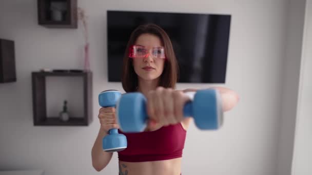 Portrait de fille confiante en lunettes de réalité virtuelle est engagé dans l'entraînement sportif avec des poids dans les mains. — Video