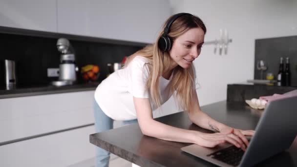 Mujer pasar tiempo con el ordenador portátil con auriculares en la cocina — Vídeos de Stock