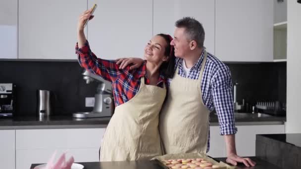 Happy ægtepar i forklæder tager en selfie i køkkenet – Stock-video