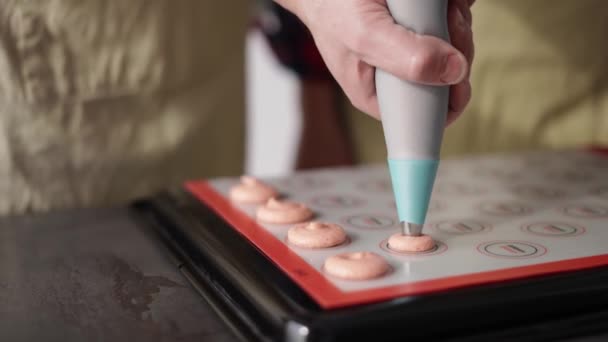Pijpen uit roze macaron mengsel op een slipmat op backing tray, professionele handen — Stockvideo