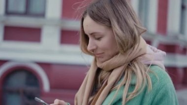 Müzik dinleyen kadın kulaklık takıyor ve sokakta akıllı telefona bakıyor.