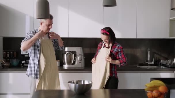 Casal alegre cozinhar juntos em casa na cozinha, colocando aventais — Vídeo de Stock