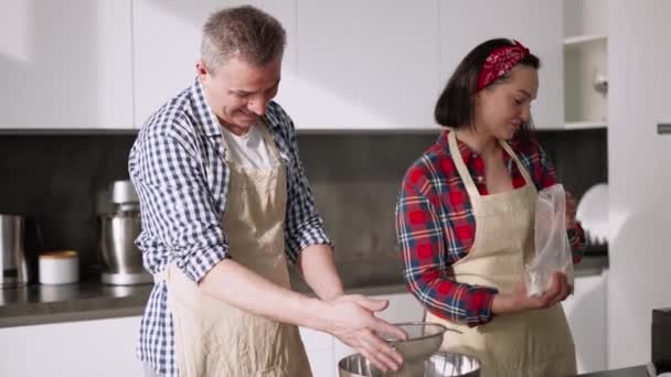 Retrato de um casal peneirando farinha para fazer pão na cozinha juntos — Vídeo de Stock