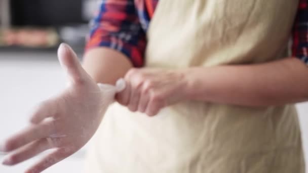 Vrouw het aantrekken van culinaire handschoenen op keuken, close up — Stockvideo