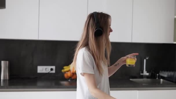 Una joven está bailando en la cocina y bebiendo jugo. — Vídeo de stock