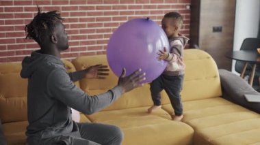 Afro-Amerikalı baba, şirin küçük çocukla evdeki kanepede oynuyor.