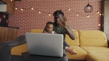 Afrika kökenli Amerikalı baba ve anaokulu çocuğu sohbet videosunda, selamlama jestinde konuşuyorlar.