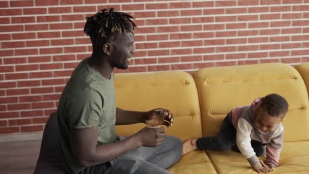 Zärtlicher afrikanischer Vater kitzelt kleinen entzückenden Sohn und hat Spaß dabei, entspannt auf dem Sofa zu lachen — Stockvideo
