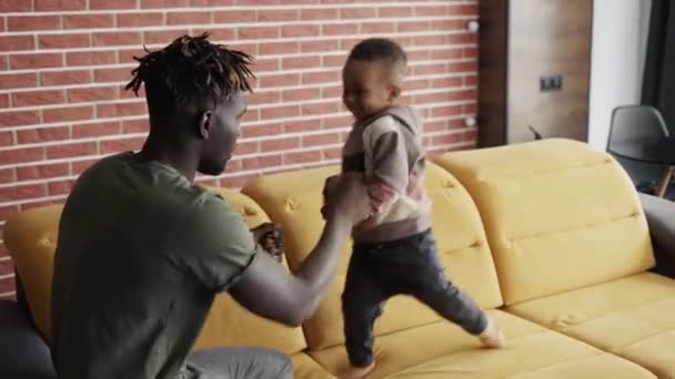 Afrikai hím és a kisfia együtt töltenek egy kis időt, a kanapén hülyéskednek. — Stock videók