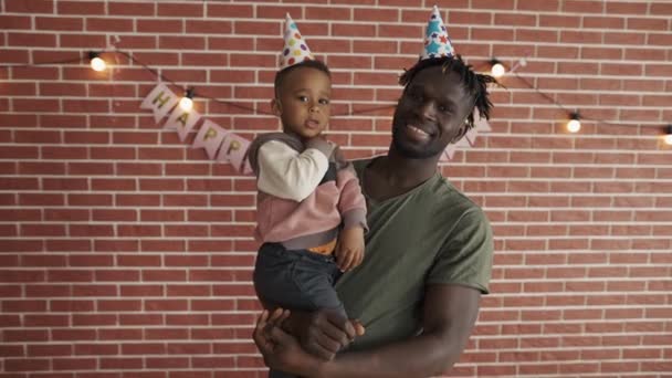 Πορτρέτο του χαριτωμένου αφροαμερικανού αγοριού στην αγκαλιά του πατέρα σε b-day καπέλα — Αρχείο Βίντεο