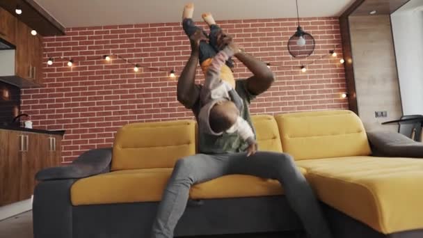 Afrikanischer Vater spielt mit kleinem entzückenden Sohn, der Spaß auf dem Sofa hat — Stockvideo