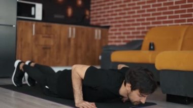 Avrupalı bir adam antrenman yapıyor, şınav çekiyor, evde bir paspasın üzerinde yatıyor.